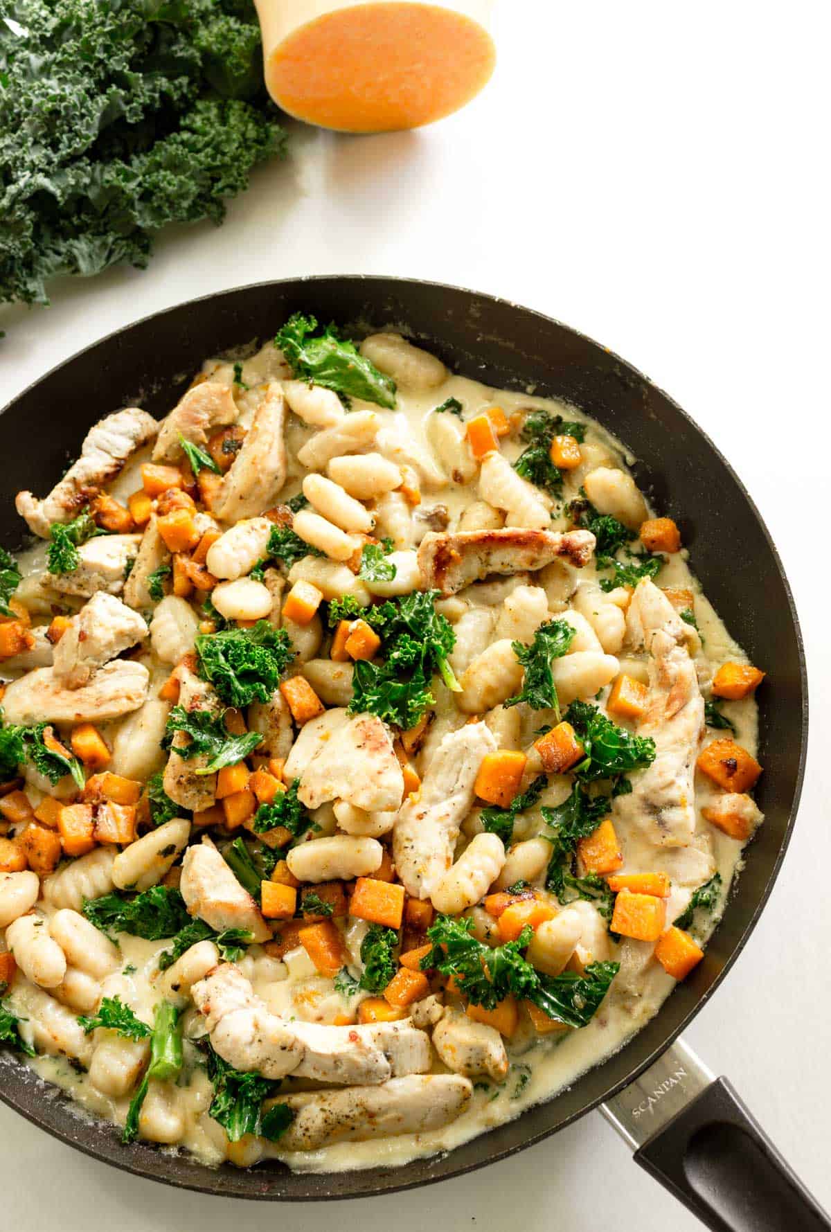 A skillet containing gnocchi in a creamy sauce with butternut squash, kale, and grilled chicken stirred in.