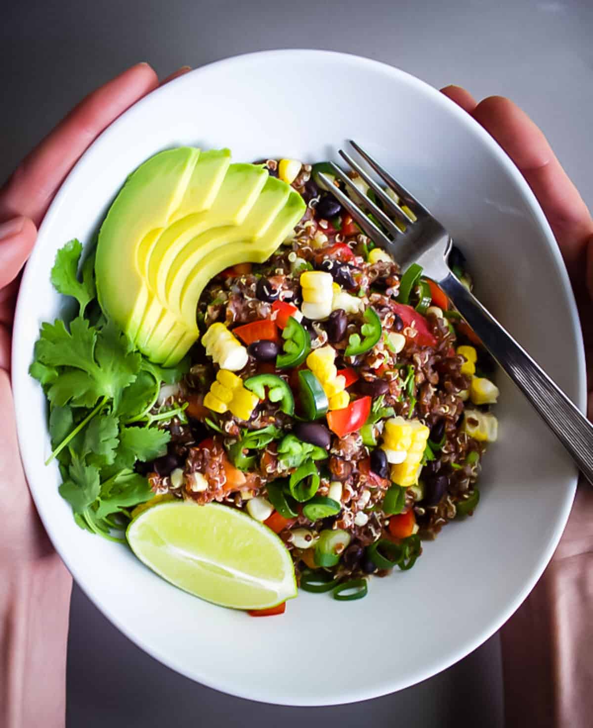 Two hands are holding a bowl of spicy red quinoa salad.