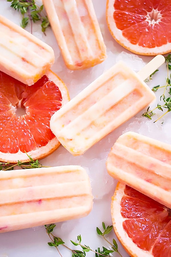 Beautiful orange marbled popsicles made from grapefruits and peaches sitona white plate with slices offresh grapfruit and sprigs of thyme.