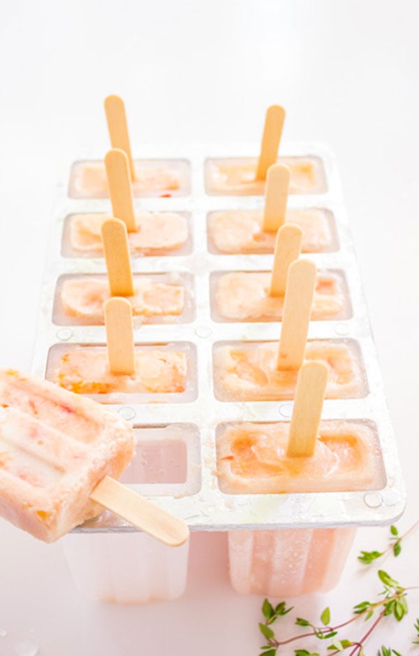 A popsicle tray with 10 frozen grapefruit peach popsicles. One popsicle has been removed and is laying on top of the tray.