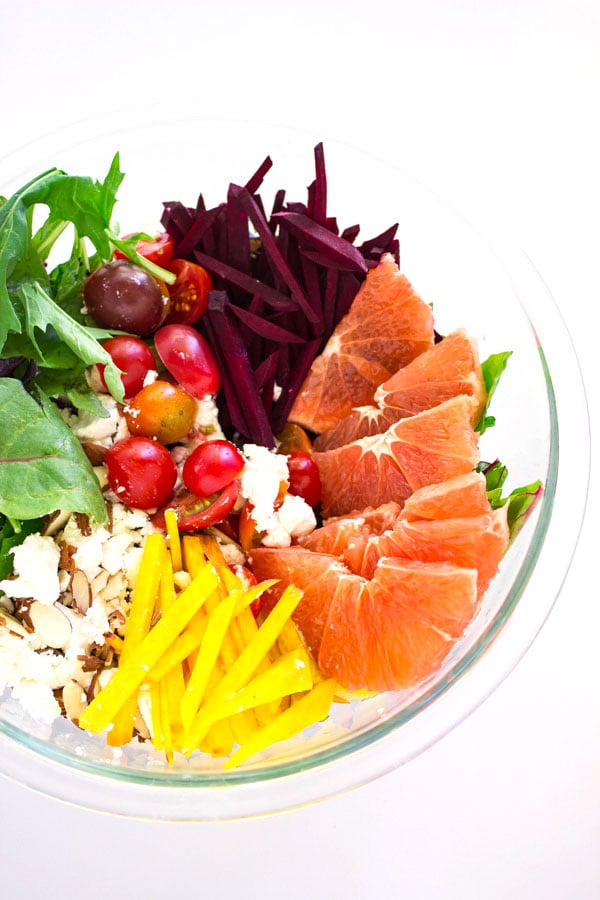 Green salad with sliced grapefruit and red and golden beets with balsamic dressing in a clear bowl.