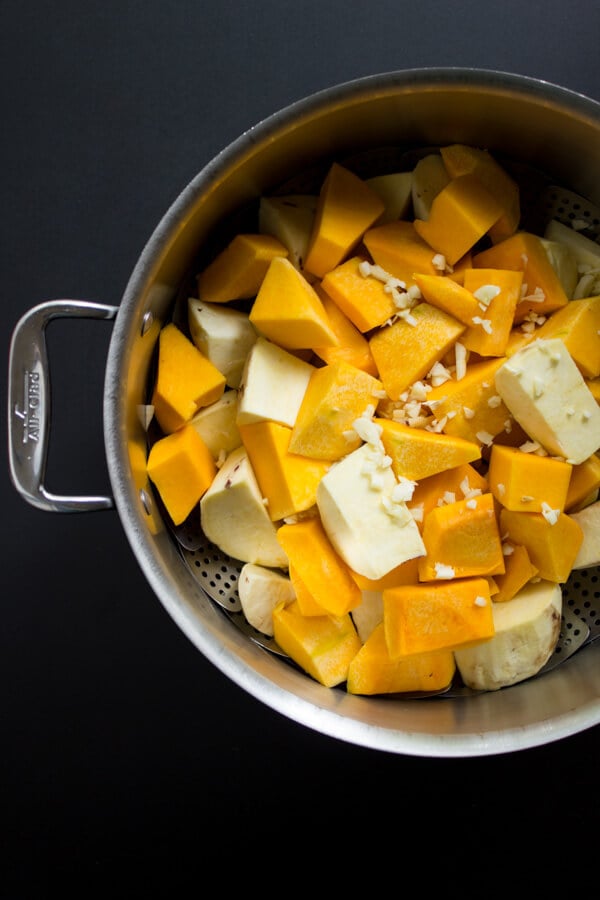 Chopped butternut squash and Japanese sweet potatoes sit in a steamer with chopped garlic on top.