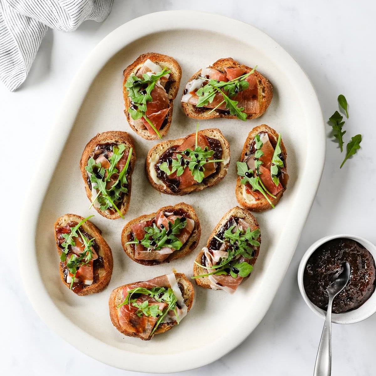 Fig and prosciutto crostini topped with arugula and balsamic reduction.