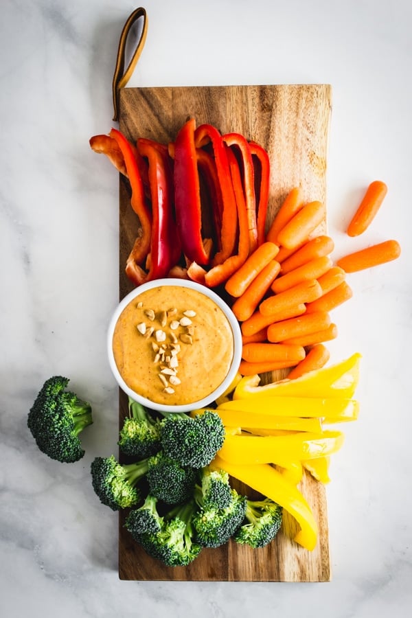 A serving board with a dish of 5-Minute Peanut Sauce and a rainbow array of veggies ready to be dipped.