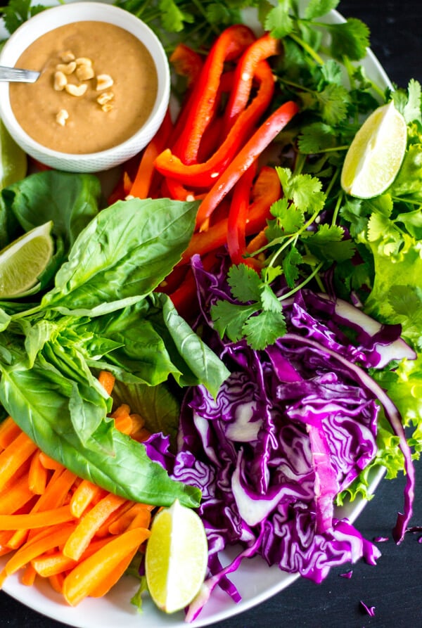 Purple cabbage, carrots, basil, cilantro, and red bell peppers spread on a plate. Peanut sauce for dipping is in a small dish.
