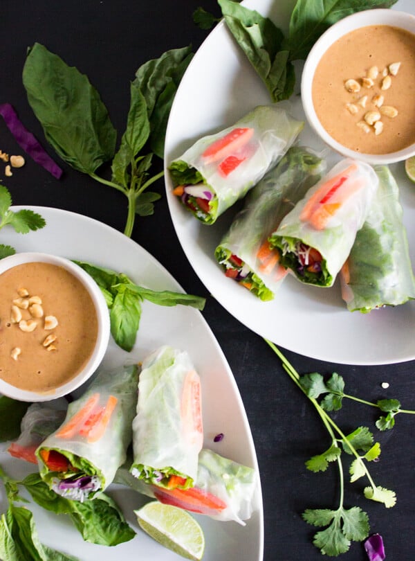 Two plates with vegan salad spring rolls and small dishes of peanut sauce for dipping are ready to be served.