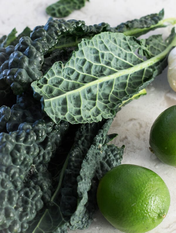 Several large lacinato kale leaves and a couple of limes on a marble countertop.