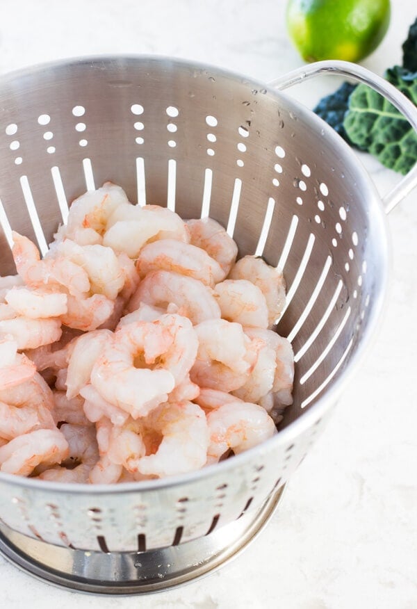 A silver colander with fresh medium-sized raw shrimp.