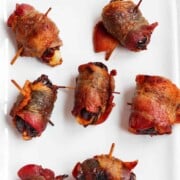 Bacon wrapped dates are served on a white rectangular plate.
