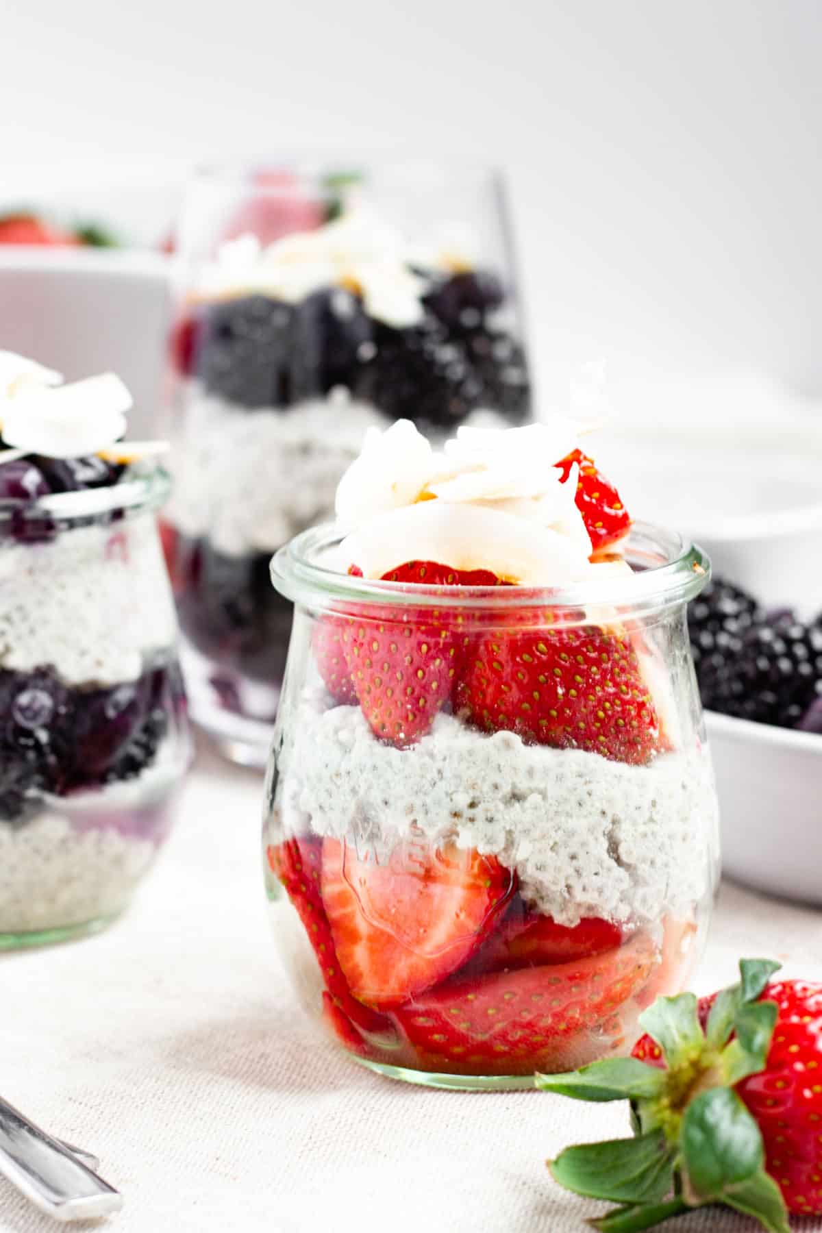Layers of fresh berries and chia pudding in a small jar topped with coconut flakes.