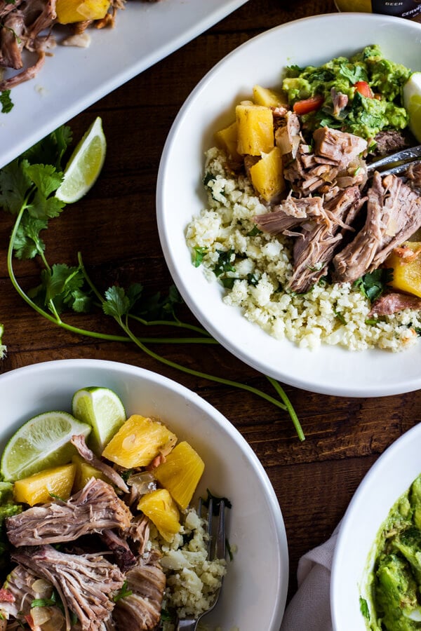 Two plates loaded with pineapple pulled pork over cilantro lime cauliflower rice. Served with lime wedges and guacamole on the side.