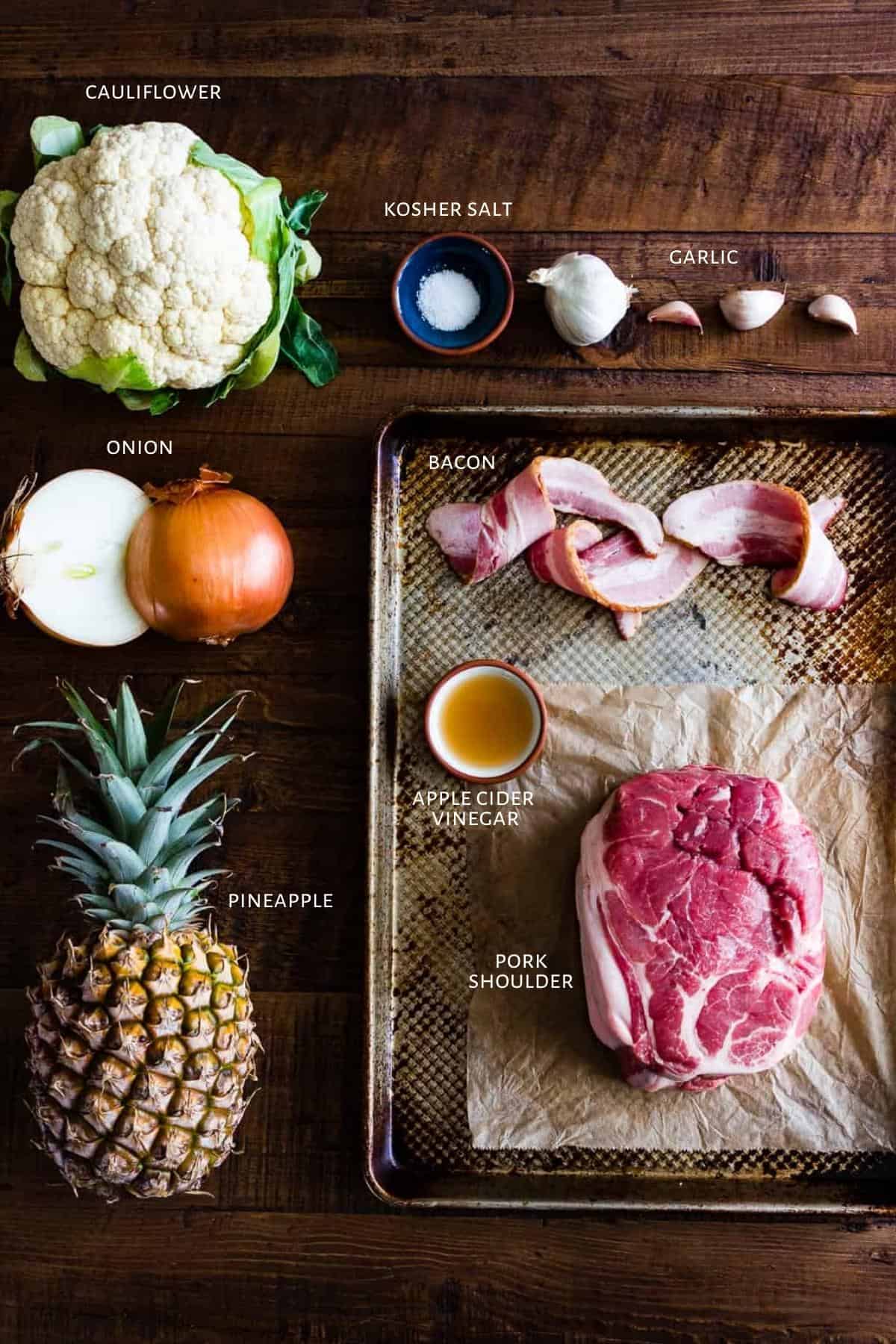 Ingredients for pineapple pulled pork are spread out on a metal pan and a wooden table.