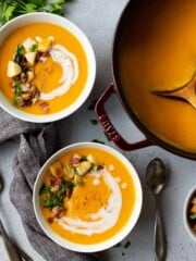 Two bowls of butternut squash soup sitting next to a pot of soup.