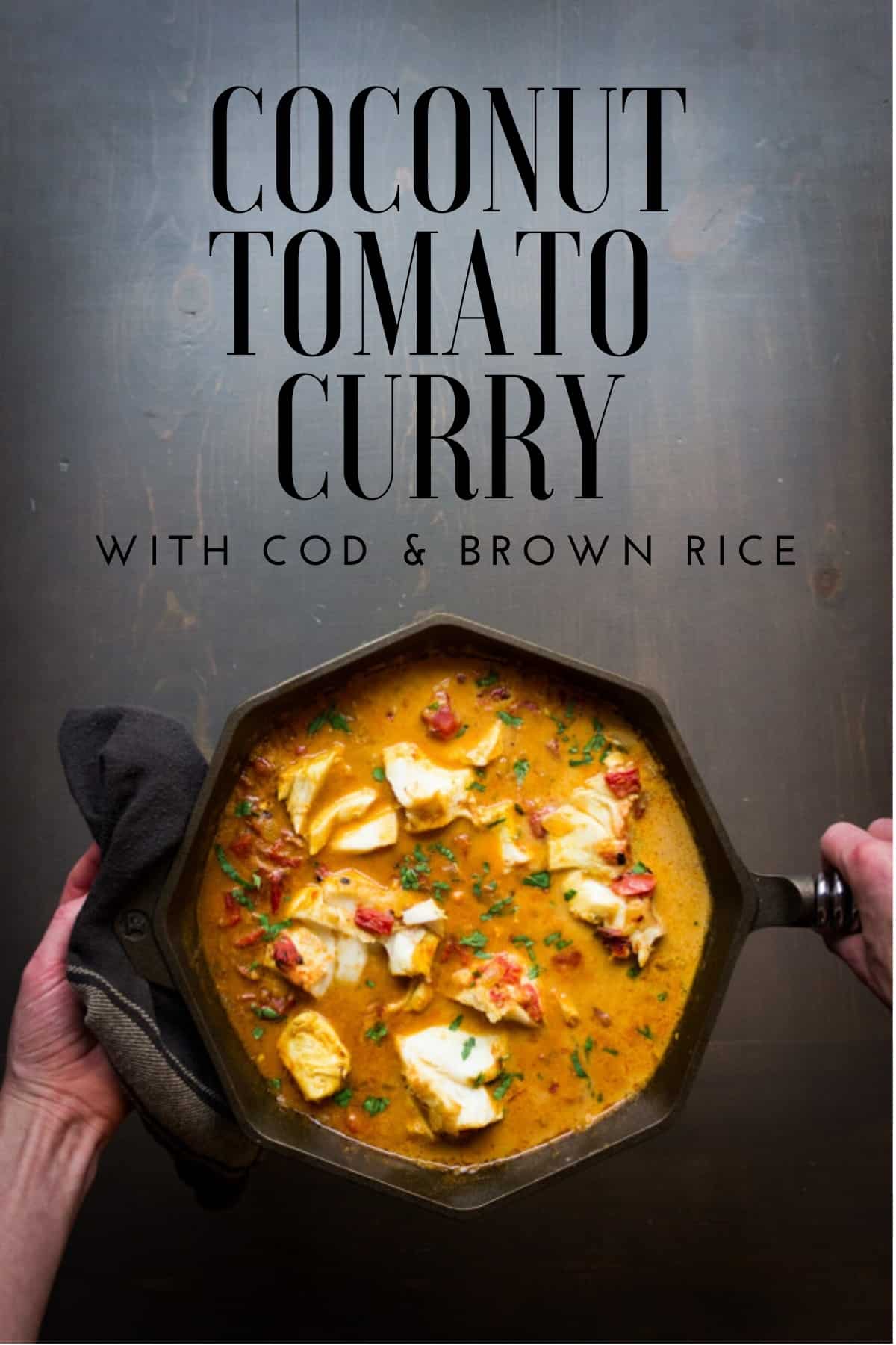Two hands holding a cast iron skillet with coconut tomato curry and cod.
