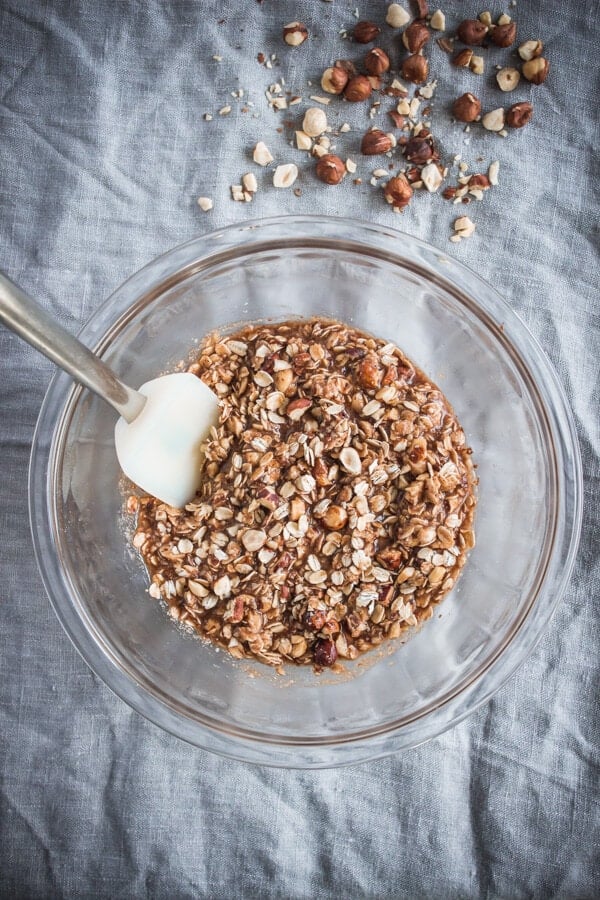 The hazelnut crisp ingredients combined in a mixing bowl with a spatula. Some chopped hazelnuts are off to the side.
