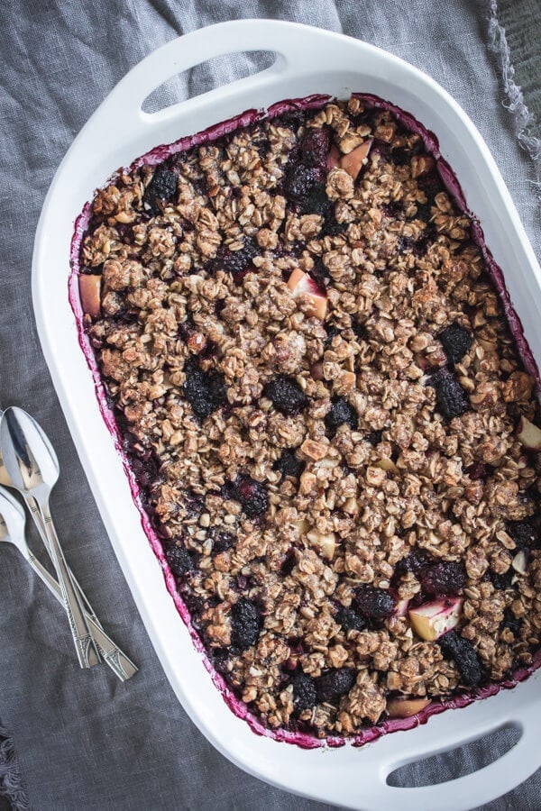 A large baking dish of blackberry apple hazelnut crisp right out of the oven with several spoons resting nearby ready to dive in to dessert.
