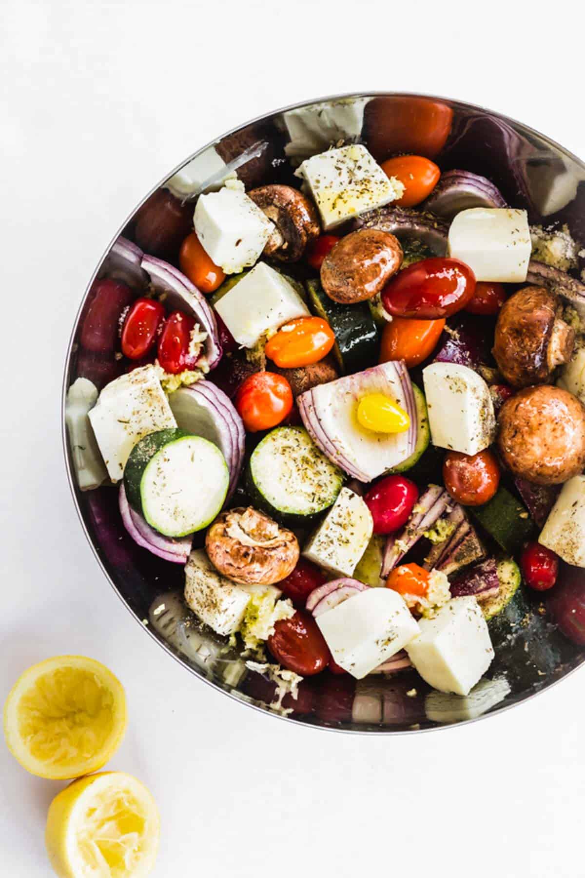 A large bowl of veggies and Halloumi cheese marinating in olive oil, lemon, and herbs.