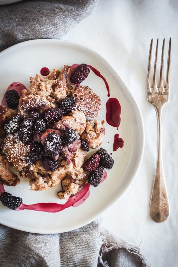 A plate of Kaiserschmarrn topped with roasted Oregon Marionberries and their juices. A silver fork rests nearby.