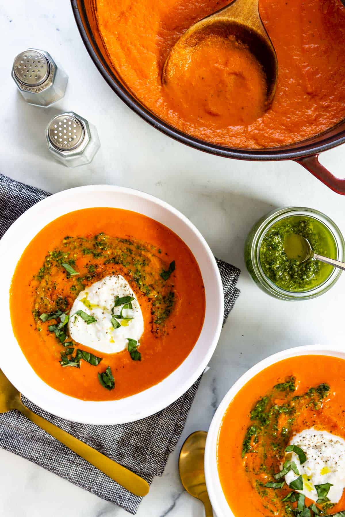 Pesto and burrata is served alongside a pot and two bowls of soup.