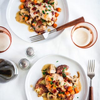 Two plates of chicken coq au vin blanc topped with crispy bacon pieces, carrots, mushrooms, and a tasty, white wine gravy-like sauce. Two rose colored glasses with a bottle of Riesling sit nearby.