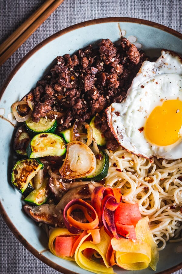 Sautéed vegetables, savory ground beef, and a fried egg are served over rice ramen.