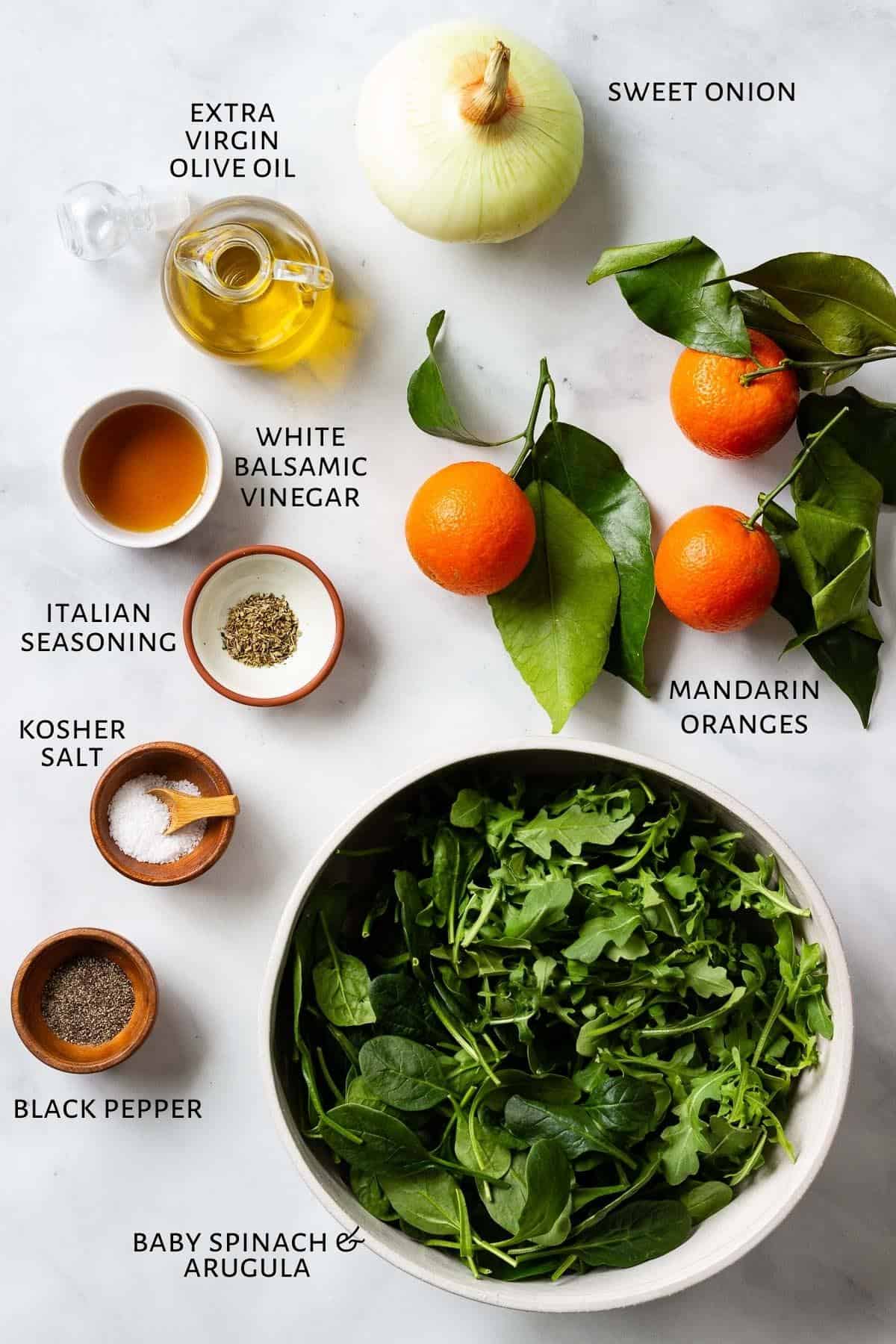Ingredients for an arugula spinach salad and winter citrus are sitting on a marble countertop.