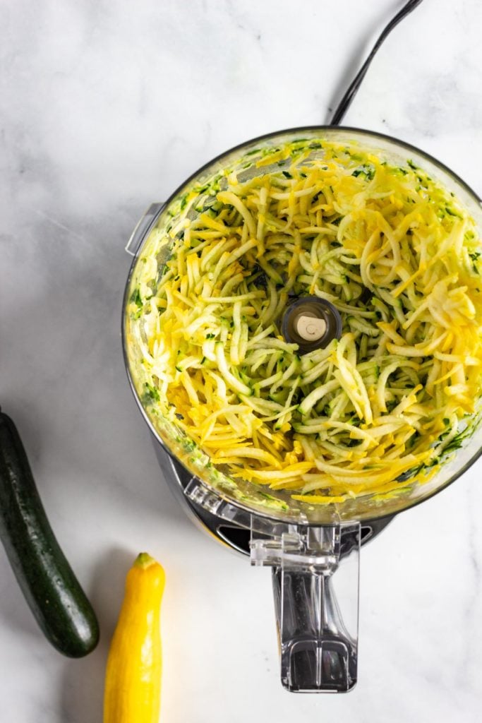 Green and yellow zucchini grated effortlessly in a food processor.