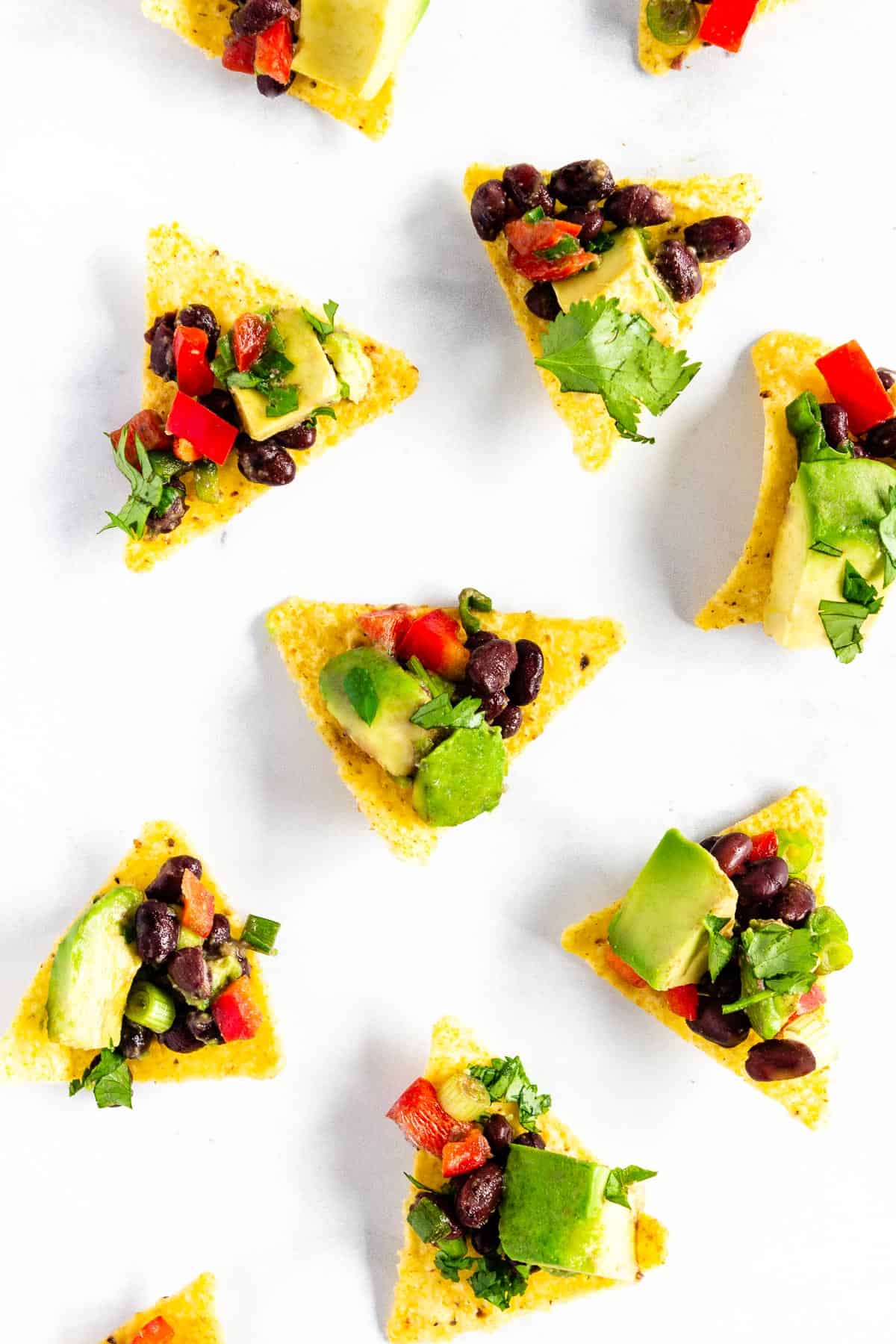 Tortilla chips topped with avocado black bean salsa sit scattered on a white countertop.