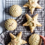 Circle and star shaped gluten-free raspberry hand pies with white chocolate drizzle rest on a cooling rack. a hand it reaching forth to grab one.