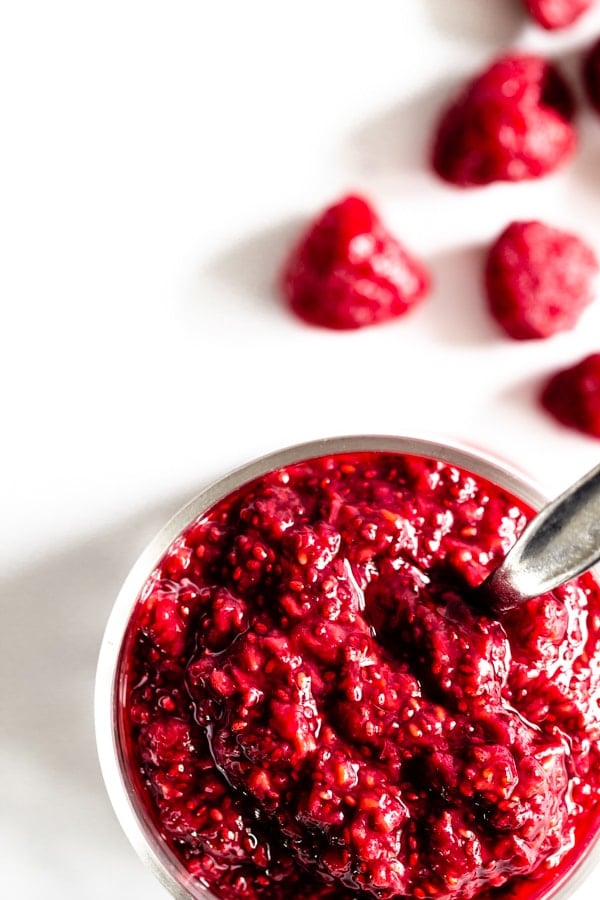 A jar of homemade raspberry chia jam with some raspberries sitting off to the side.