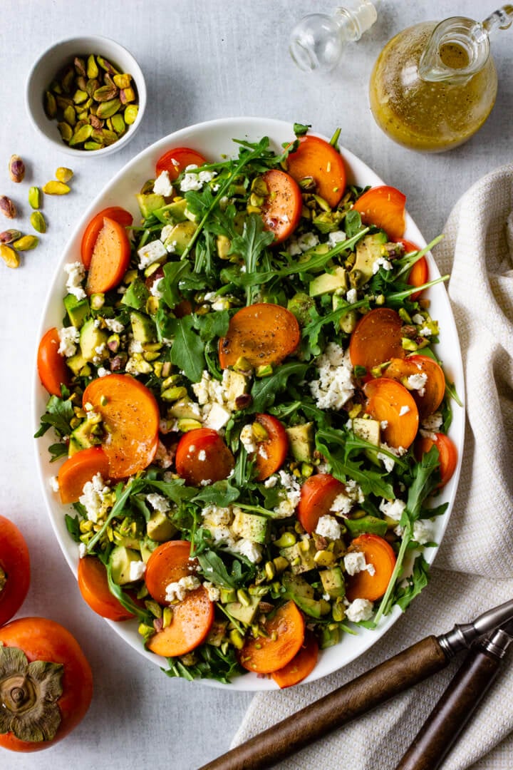 A beautiful persimmon arugula salad topped with chopped pistachios, feta, and a simple lemon vinaigrette.
