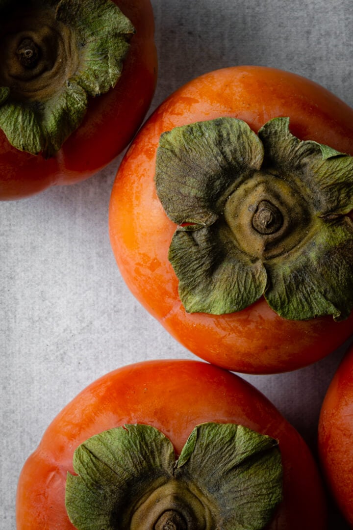 Bright orange-red persimmons sitting on a gray countertop.