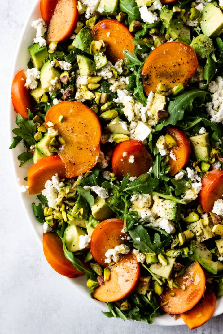 Quartered persimmons are tucked into a pile of arugula and topped with crumbled feta and chopped pistachios.