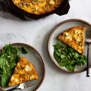 Two servings of baked frittata served with a side salad. A cast iron skillet with the remaining frittata sits off to the side.
