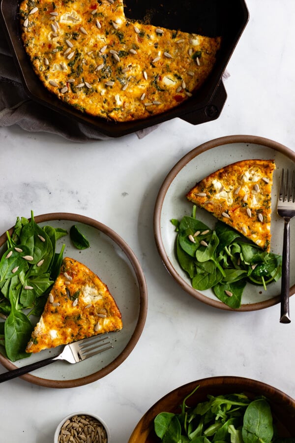 Two servings of baked frittata served with a side salad. A cast iron skillet with the remaining frittata sits off to the side.