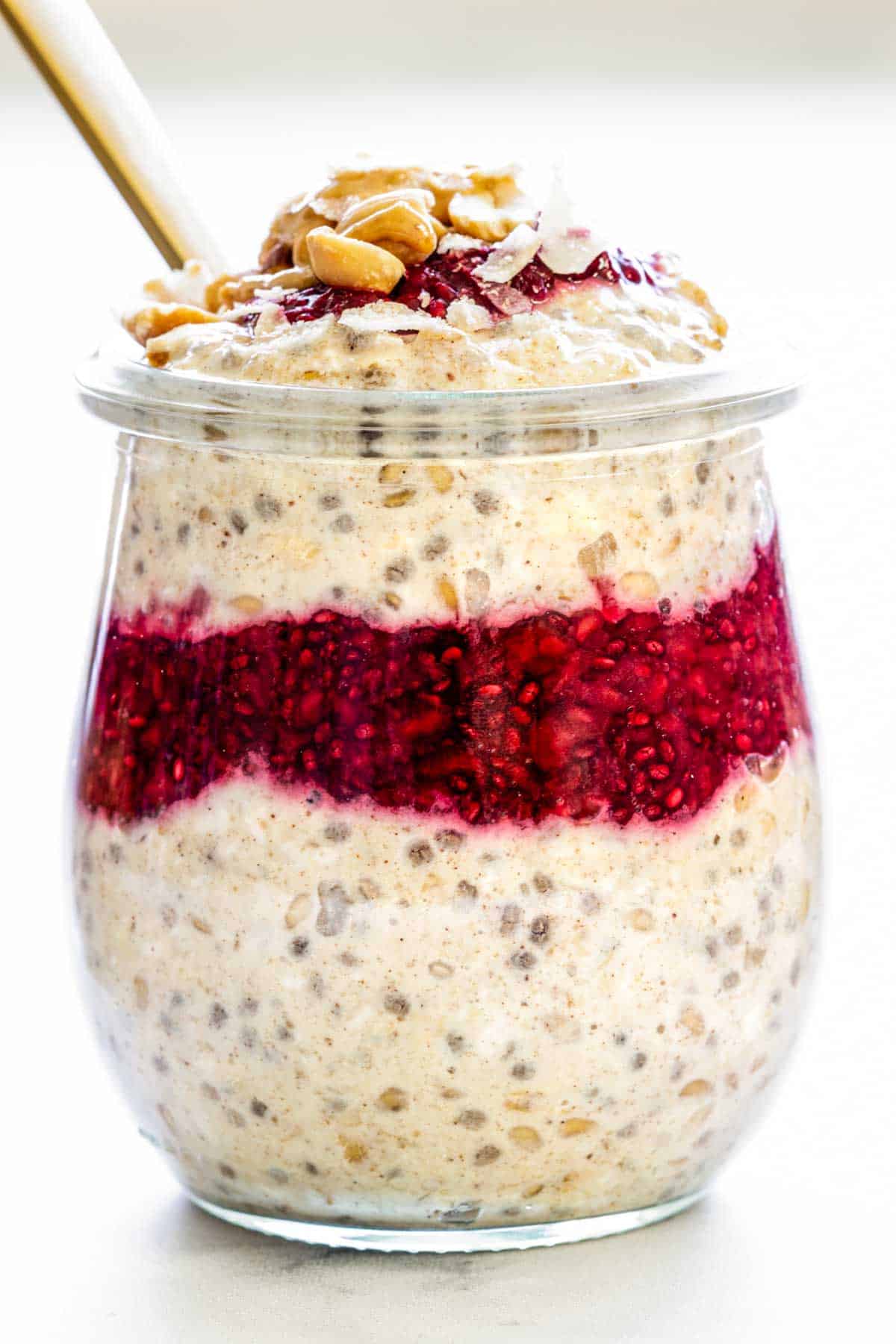 A jar of overnight oats with greek yogurt, berries, and peanut butter. Topped with chopped peanuts, berry chia jam, and toasted coconut flakes.