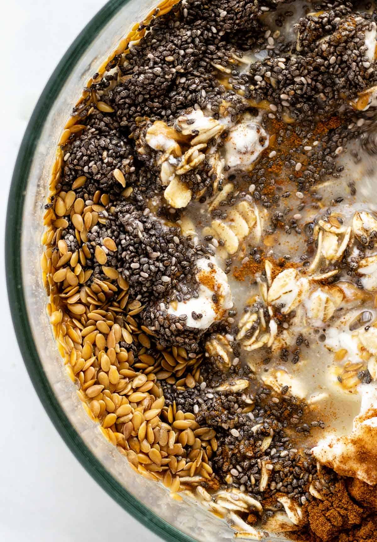A bowl of healthy overnight oats ingredients like flax seeds, chia seeds, cinnamon, rolled oats, oatmilk, and greek yogurt.