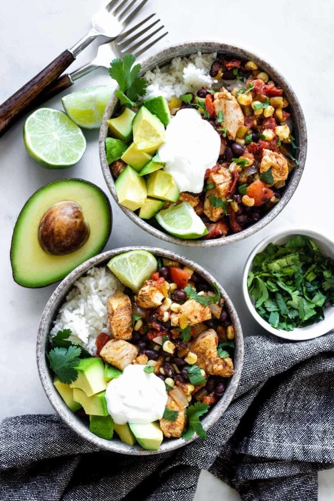 Two bowls of southwest chicken and rice topped with cilantro, avocado, and sour cream. Served with lime wedges.