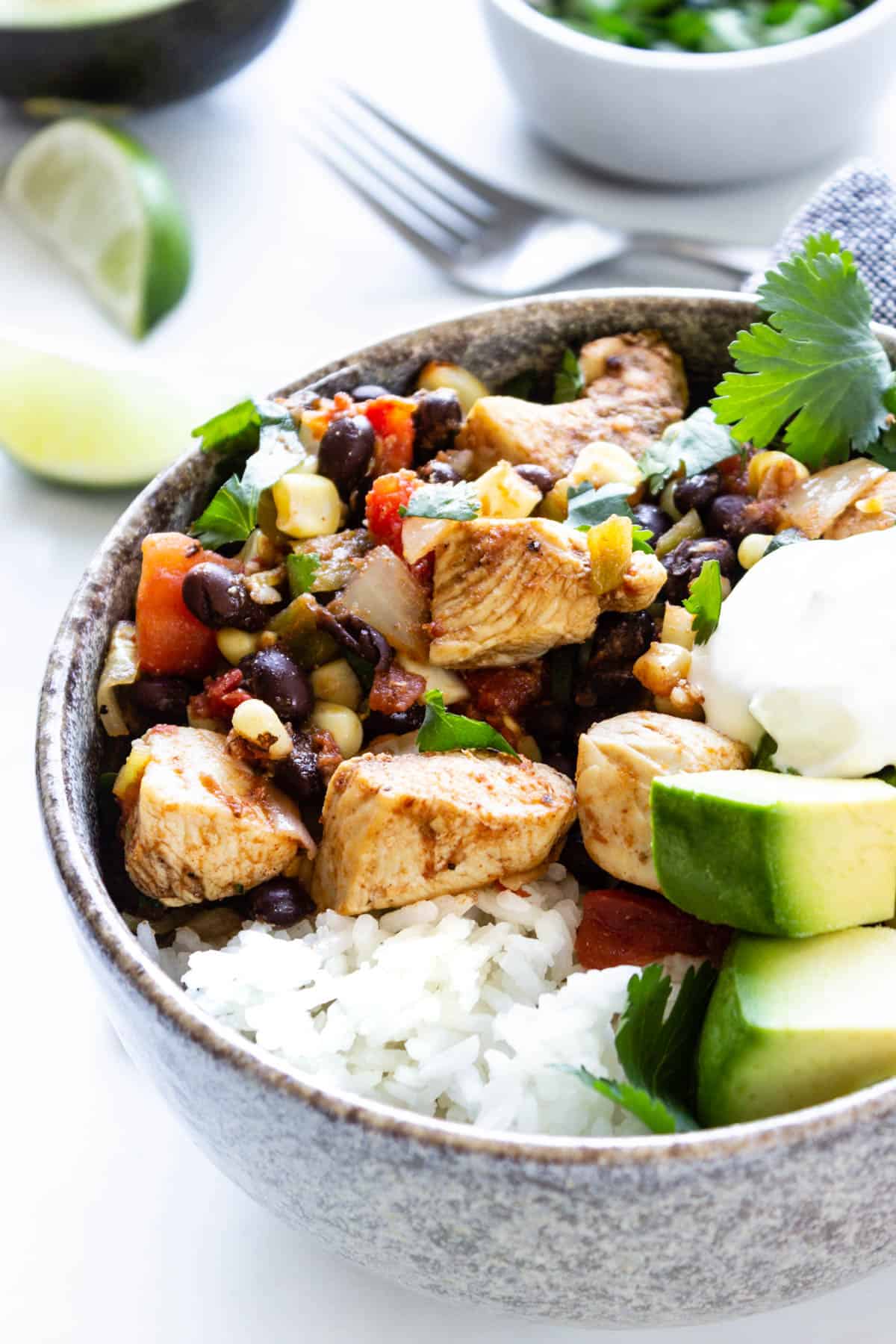 A close-up view of a comforting southwest chicken rice bowl topped with avocado, sour cream, and cilantro.