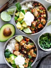 Two bowls of southwest chicken and rice topped with cilantro, avocado, and sour cream. Served with lime wedges.