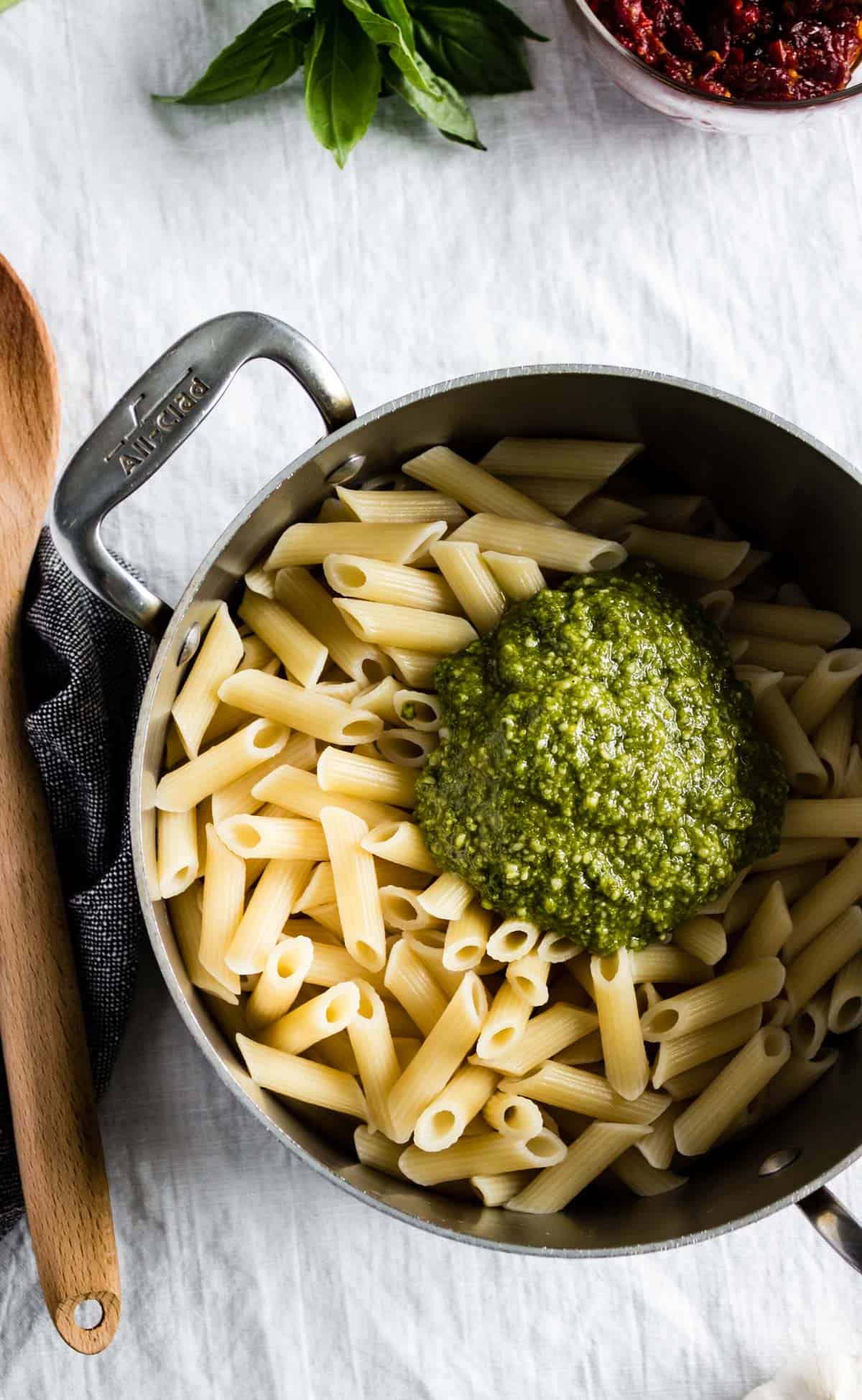 A pot of pasta with a large dollop of homemade basil pesto ready to be stirred in.