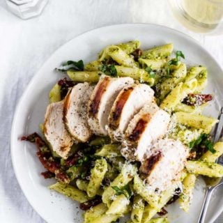 A plate of creamy pesto pasta topped with sun-dried tomatoes and grilled chicken. A perfect meal for any night!