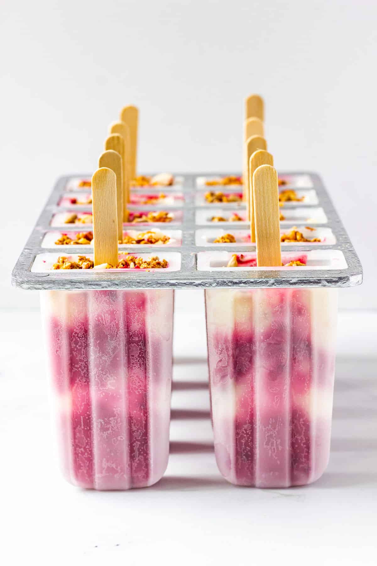 A popsicle mold filled with berry yogurt popsicles wits on a marble countertop.