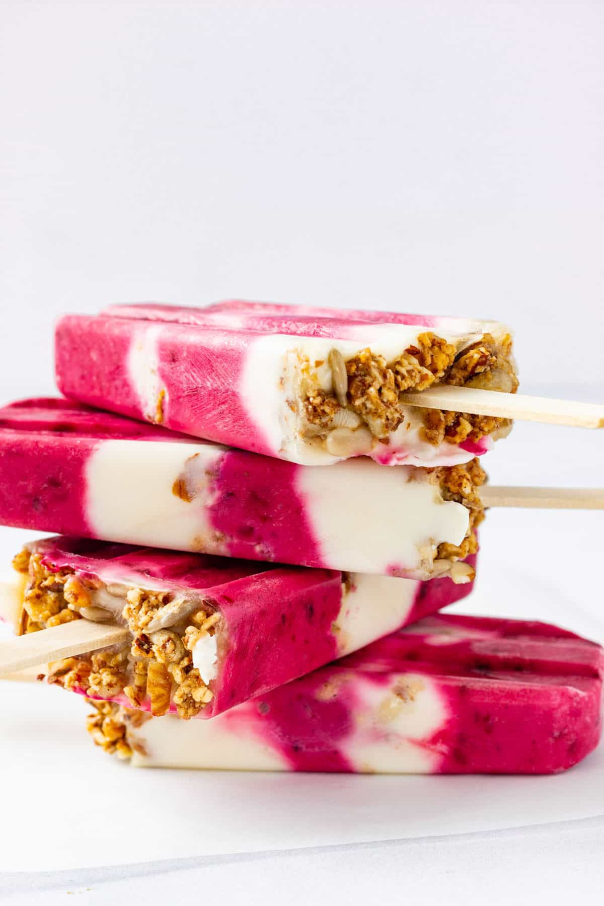 Four berry yogurt popsicles with granola are stacked on top of each other.