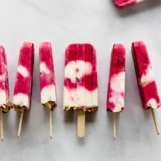 Berry yogurt popsicles are lined up horizontally on a marble countertop.