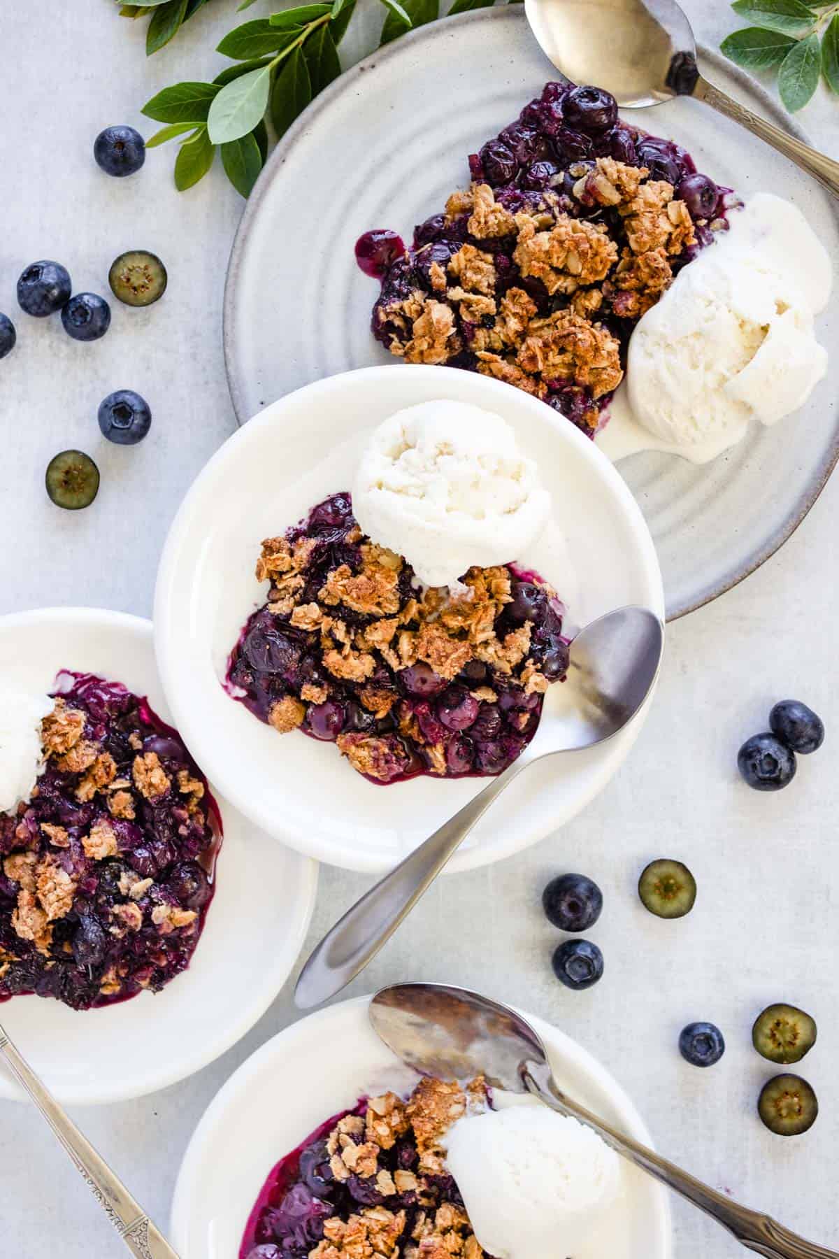 Four plates with blueberry crisp are topped with vanilla ice cream and ready to be served.