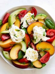 Slices of peach, tomato, and avocado are topped with burrata, basil and olive oil.