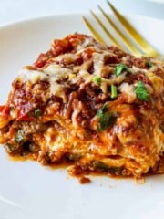 A serving of lasagna on a white plate with a gold fork.