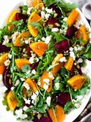 Arugula is topped with roasted beets and butternut squash and served on a white platter.