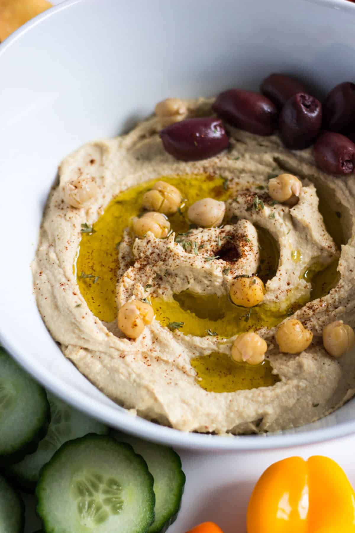 A bowl of hummus topped with chickpeas, olives, and seasoning.